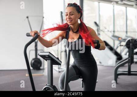 Frau Übung Fahrrad Fitness-Studio Radfahren Training Fitness. Fitness-Frau mit Air Bike Cardio-Training. Athlet Mädchen Sportswear Radfahren Indoor-Fitness-Studio Ausübung seiner Beine. Funktionsübergreifende Schulung. Stockfoto