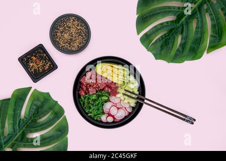Draufsicht auf Thunfisch-Poke-Schüssel mit Reis, Avocado, Wakame, Rettich und Gurke auf rosa Hintergrund Stockfoto