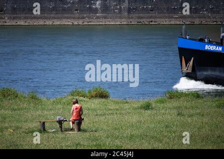 Köln, Deutschland. Juni 2020. Eine Frau genießt die Sonne auf den Pollerwiesen am Rheinufer, wenn ein Frachtschiff vorbeifährt. Quelle: Henning Kaiser/dpa/Alamy Live News Stockfoto
