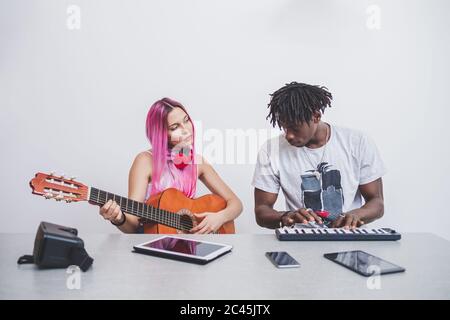 Junge Frau mit langen rosa Haaren und junger Mann mit kurzen Dreadlocks Gitarre und Keyboard spielen. Stockfoto