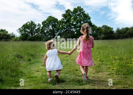 Rückansicht von zwei jungen Mädchen, die Hand in Hand über eine Wiese gehen. Stockfoto