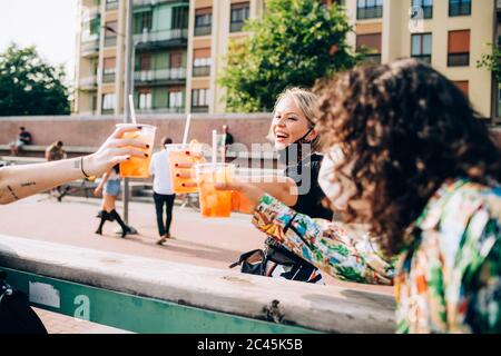 Drei junge Frauen sitzen draußen auf einer Bank, toasten. Stockfoto