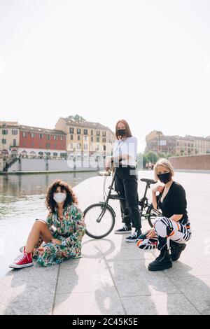 Drei junge Frauen, die Gesichtsmasken während des Corona-Virus tragen, stehen draußen am Flussufer und schauen auf die Kamera. Stockfoto