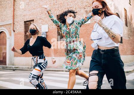 Drei junge Frauen tragen Gesichtsmasken während des Corona-Virus und laufen über eine Fußgängerüberführung in einer Straße. Stockfoto