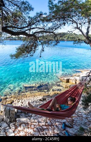 Frau, die SMS mit Smartphone in Hängematte auf der Insel mljet, kroatien Stockfoto