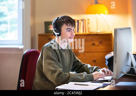 Junge mit Kopfhörern, die am Schreibtisch vor dem Computer sitzen und studieren. Stockfoto