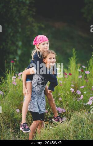 Junge Tween Mädchen tragen Freund Huckepack in wilden Blumenwiese Stockfoto