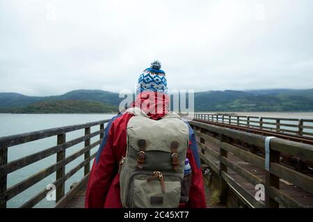 Rückansicht des Wanderers, der über die Barmouth Bridge geht, einem hölzernen Eisenbahnviadukt über die Mündung des Flusses Mawddach, Barmouth Stockfoto