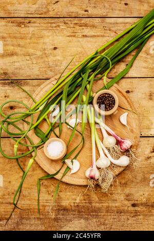 Set von Zutaten für das Einlegen von Knoblauch Pfeile. Reifes Gemüse, Kräuter, Meersalz, Gewürze. Alte Holztisch, Schneidebrett Stockfoto