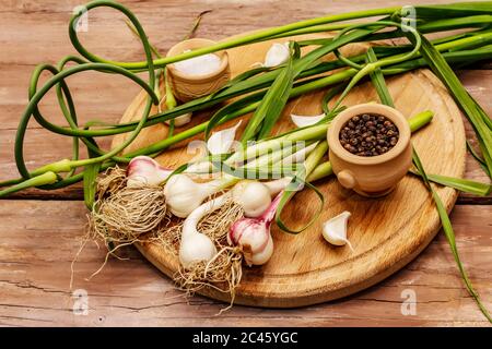 Set von Zutaten für das Einlegen von Knoblauch Pfeile. Reifes Gemüse, Kräuter, Meersalz, Gewürze. Alte Holztisch, Schneidebrett Stockfoto