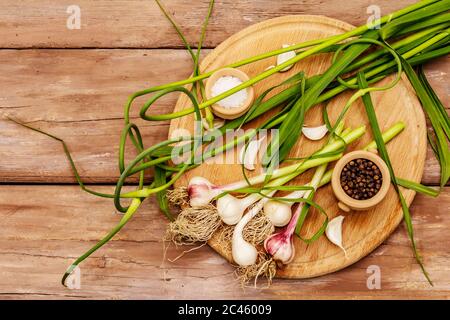 Set von Zutaten für das Einlegen von Knoblauch Pfeile. Reifes Gemüse, Kräuter, Meersalz, Gewürze. Alte Holztisch, Schneidebrett Stockfoto