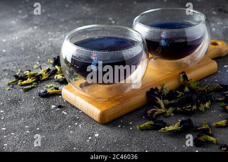 Natürlicher blumiger blauer Tee in hitzebeständigen Gläsern auf dunklem Hintergrund Stockfoto