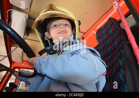 Kleiner Junge, der wie ein Feuerwehrmann agiert. Junge sitzt in einem echten Feuerwehrauto. Stockfoto