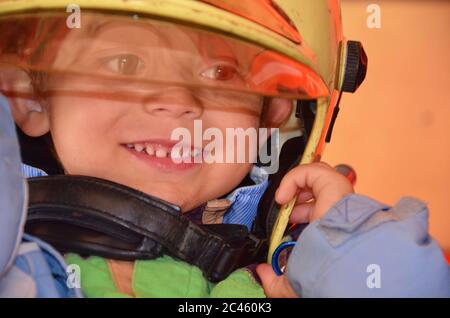 Kleiner Junge, der wie ein Feuerwehrmann agiert. Junge, der Feuerhelm auf den Kopf setzt. Träumen von zukünftigen Beruf. Brandschutz, Lebensschutz Unterricht. Nahaufnahme Stockfoto