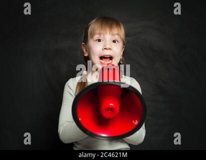 Kleines Mädchen, das durch ein Megaphon auf schwarzem Hintergrund schreit. Kind mit Lautsprecher Stockfoto