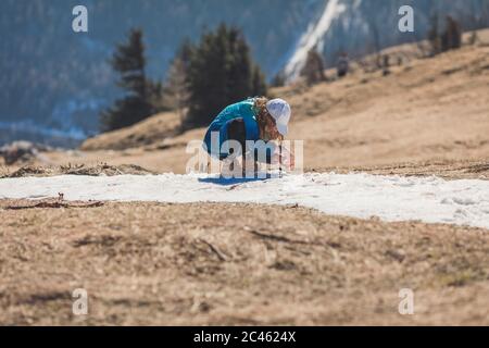 Junges Mädchen, zwischen Alter, trägt Sonnenkappe und Sonnenbrille spielen mit schmelzendem Schnee in alpiner Landschaft Stockfoto