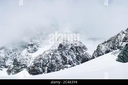 Fantastische Landschaft von felsigen Bergen mit Schnee bedeckt. Panoramablick auf schneebedeckte Bergfelsen mit pyramidenförmigem Gipfel unter nebligen Himmel. Konzept der felsigen Hügel, Natur Schönheit und Winter. Stockfoto