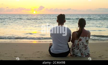 Ein reizendes junges Paar sitzt am leeren Meeresstrand und beobachtet den Sonnenuntergang im tropischen Resort am Abend mit Blick auf die Rückseite Stockfoto