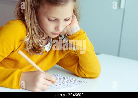 Portrait von dorable aber müde Teenager-Mädchen lösen Sudoku am Schreibtisch in der Schule oder zu Hause. Blick von oben Stockfoto
