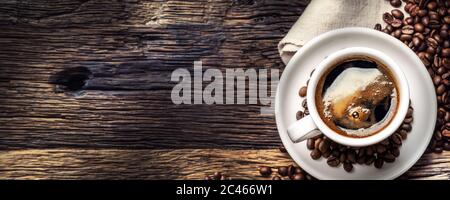 Schwarzer Kaffee in Porzellanbecher mit verstreuten Bohnen auf rustikalem Holztisch Stockfoto
