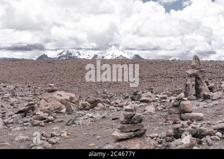 Wunderschöne trockene Landschaft mit Steinhaufen (apacheta), verschneiten Bergen und bewölktem Himmel in Salinas und Aguada Blanca National Reserve. Peruanischen Altiplano Stockfoto