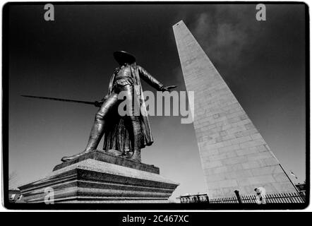 Bunker Hill Monument und Statue von Dr. Joseph Warren Boston USA 1988 das Bunker Hill Monument wurde errichtet, um der Schlacht von Bunker Hill zu gedenken, die zu den ersten großen Schlachten zwischen britischen und Patriot-Truppen im amerikanischen Revolutionskrieg gehörte, die dort am 17. Juni 1775 ausgetragen wurden. Der 221 Fuß (67 m) große Granitobelisk wurde zwischen 1825 und 1843 in Charlestown, Massachusetts, errichtet, wobei Granit aus dem nahe gelegenen Quincy über die eigens dafür gebaute Granite Railway zum Standort transportiert wurde, gefolgt von einer Fahrt mit dem Lastkahn. Es gibt 294 Stufen nach oben. Eine Ausstellungshütte, die in der Nähe der Basis des Denkmals in der gebaut wurde Stockfoto