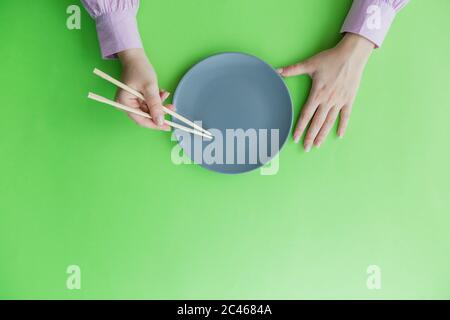 Flache Lage der weiblichen Hand halten Essstäbchen und leere Platte isoliert auf grünem Hintergrund. Stockfoto