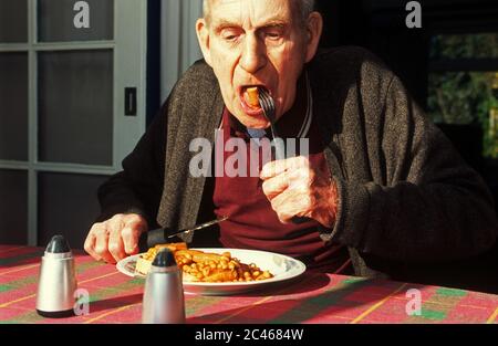 Rentner im Alter, der zum Frühstück gebackene Bohnen und Würstchen isst Stockfoto