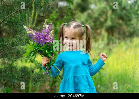 Kleines schönes Mädchen im Wald mit einem Blumenstrauß von Lupinen Stockfoto