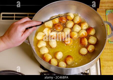 Frau fritiert runde Knabbergebäck oder kleine Donuts in heißem Öl. Stockfoto