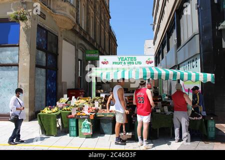 Ein Foto eines Obst- und Gemüsehändlers in der Cardiff Queen Street. Kunden, die Social Distancing-Maßnahmen verfolgen, stehen in der Warteschlange. Bauernmarkt. Stockfoto