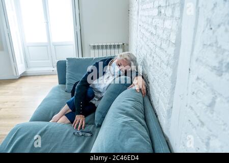 Einsame depressive ältere Witwe Frau mit Schutzmaske weinend auf Couch isoliert zu Hause, traurig und besorgt vermissten Mann und Familie in COVID-19 Deat Stockfoto