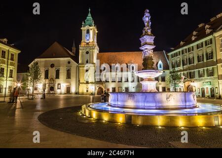 BRATISLAVA, SLOWAKEI - 29. April 2016: Altes Rathaus in Bratislava, Slowakei bei Nacht mit einem Teil des Maximilians-Brunnens im Vordergrund. Menschen können Stockfoto