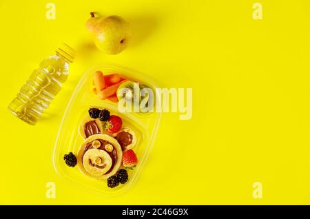 Kinderessen in Lunchboxen mit Wasser und Birne auf gelbem Hintergrund. Stockfoto