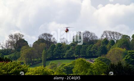 Red and Yellow Helicopter G ORKY schwebt tief in der Nähe von Häusern, Burley-in-Wharfedale, Großbritannien Stockfoto