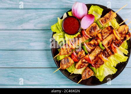 Hähnchenkebab auf Holzspieß mit Salat und heißer Sauce. Draufsicht. Stockfoto