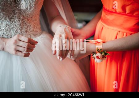 Brautjungfer in orange Kleid hilft Braut, Armband zu tragen Stockfoto