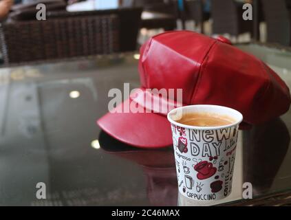 Heißer Kaffee in Papierbecher mit verschwommener roter Kappe auf dem Tisch Stockfoto
