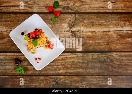 Kuchen mit frischen Beeren auf weißem Teller auf Holzhintergrund. Stockfoto