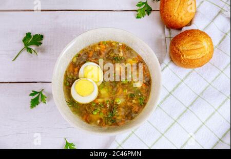 Grüne Gemüsesuppe mit Ei und knusprigen Brötchen auf Holzgrund. Stockfoto