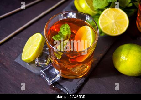 Frischer Cocktail Cuba Libre oder Whiskey Cola Cocktail mit braunem Rum, Cola, Minze und Limette auf schwarzem Hintergrund. Long Island Iced Tea Cocktail. Stockfoto