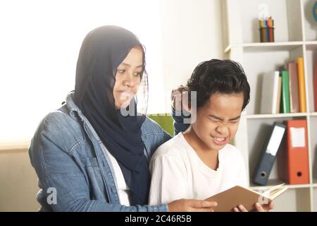 Asiatische muslimische Mutter angy und bestrafen ihren Jungen durch Ziehen sein Ohr wegen faul in seinem Studium, Mutter zwingen ihr Kind zum Lesen Buch, missbräuchlich Kind nicht wollen Stockfoto