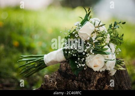 Der Brautstrauß aus weißen Rosen und grünen Blättern, wunderschön mit weißem Satinband verziert, liegt an einem Sommertag auf dem Gras. Hochzeitsthema. Stockfoto