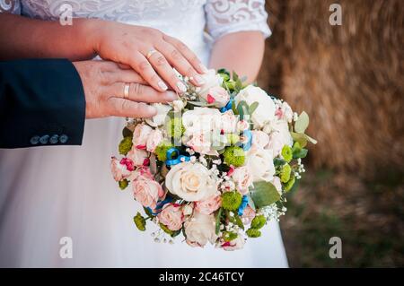 Hände des Bräutigams und der Braut liegen auf dem Blumenstrauß Stockfoto