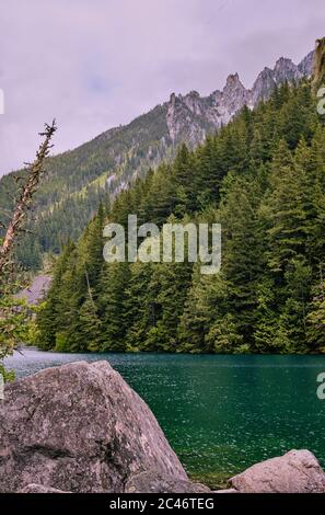 Smaragdgrünes Wasser des Lindeman Lake in Chilliwack, Provincial Park Ruhe unter steilen bewaldeten Hängen, Felsbrocken und schroffen Berggipfeln Stockfoto