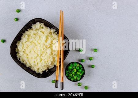 Gekochter Reis in schwarzer Schüssel mit Essstäbchen auf weißem Hintergrund. Stockfoto