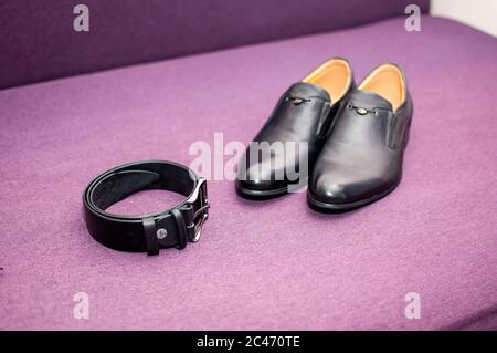 Schwarzer Gürtel und schwarze Schuhe auf dem lila Sofa Stockfoto