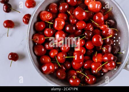 Frische Süßkirschen in einer Sieb-Schüssel mit Wassertropfen auf weißem Hintergrund. Draufsicht. Stockfoto