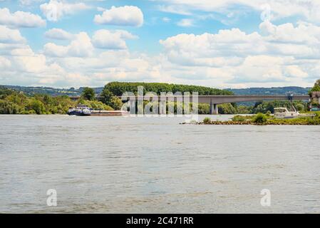 Betonstraßebrücke auf der Autobahn über den Fluss in Westdeutschland, sichtbarer, fließender Frachtschiff, im Hintergrund blauer Himmel und wolkenverwitterte Wolken Stockfoto