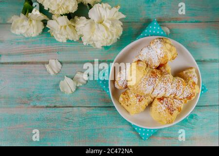 Hausgemachte Blätterteig-Kegel mit Karamell-Creme auf Holzhintergrund mit Blumen gefüllt. Stockfoto